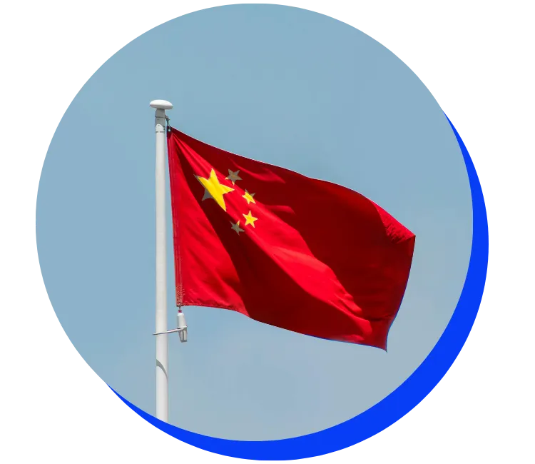 Chinese flag waving in the wind against a clear blue sky. The flag is red with five yellow stars in the upper left corner.