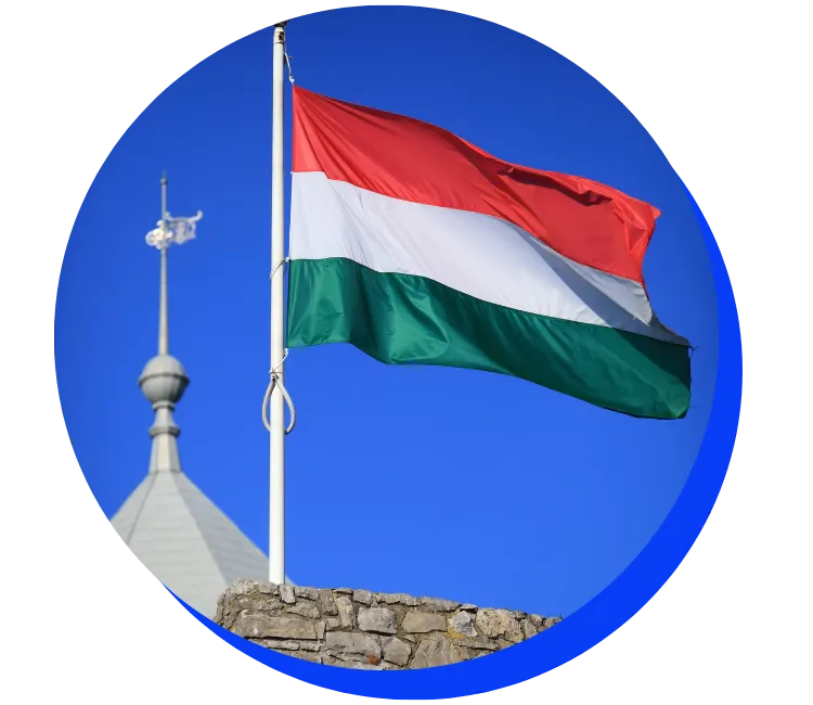 Hungarian flag flying in front of a blue sky, with a building dome visible in the background. The flag has horizontal stripes of red, white, and green.